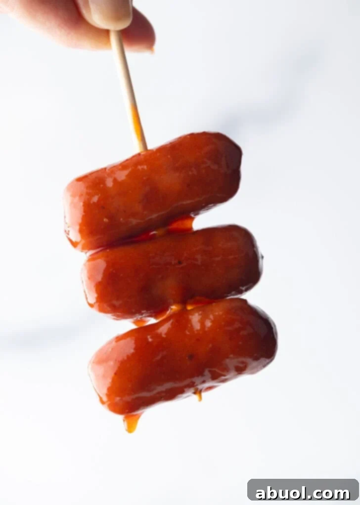 Hand holding a skewer with 3 little smokies.