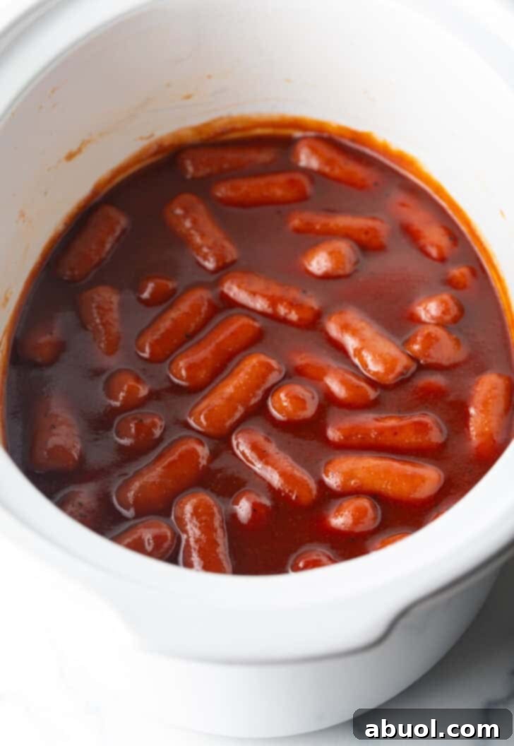 Little smokies in barbecue sauce in a white crock pot.