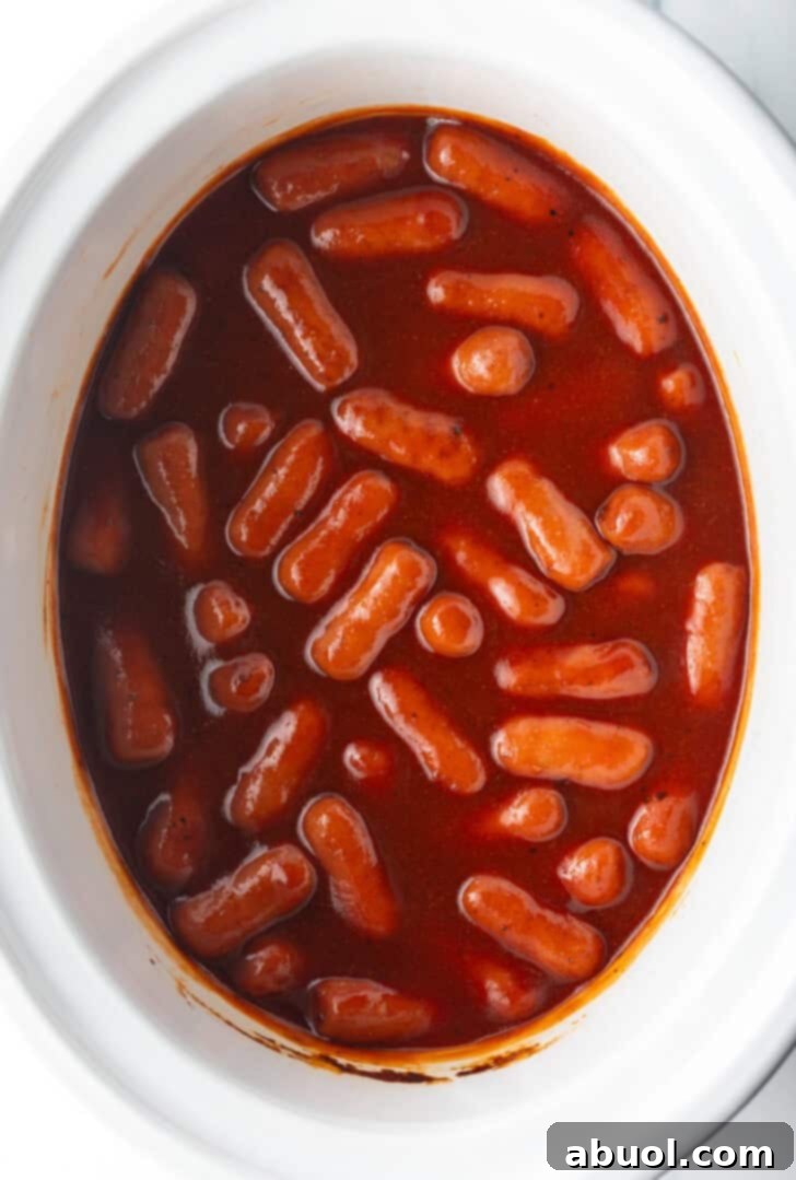 Top down view little smokies in barbecue sauce in a white crock pot.