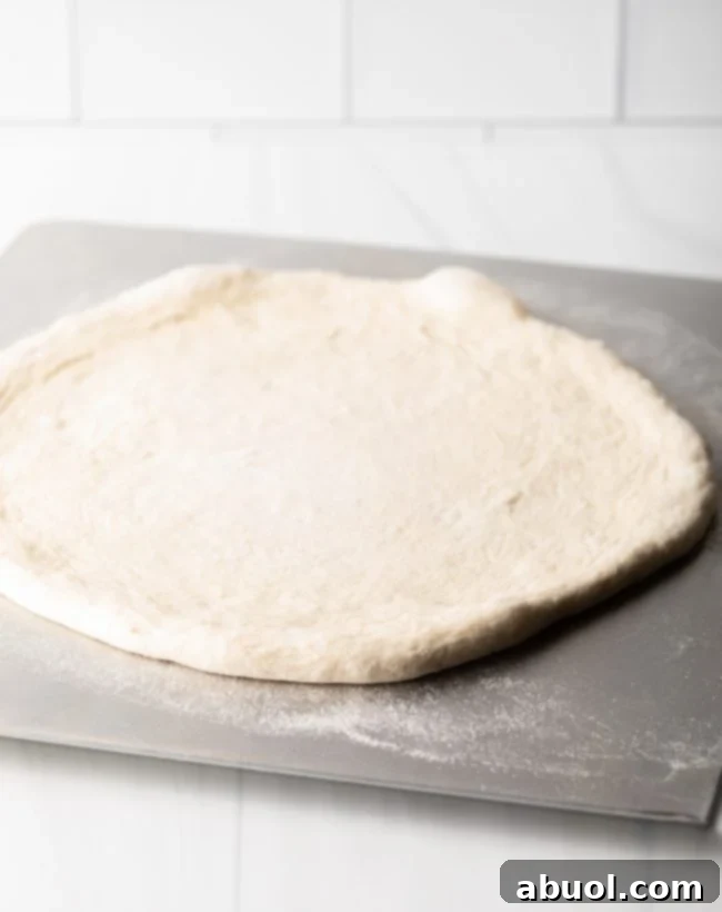 Crafting Perfect Neapolitan Pizza Dough 12 A circle of Neapolitan pizza dough spread on a metal baking sheet.