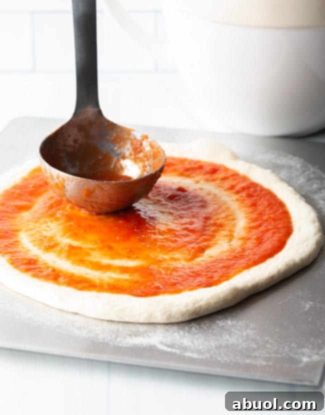 Crafting Perfect Neapolitan Pizza Dough 13 Using a metal ladle to smear tomato sauce across homemade pizza dough.