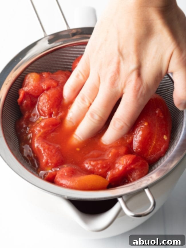 Crafting Perfect Neapolitan Pizza Dough 10 Hand smooshing whole canned tomatoes through a sieve.