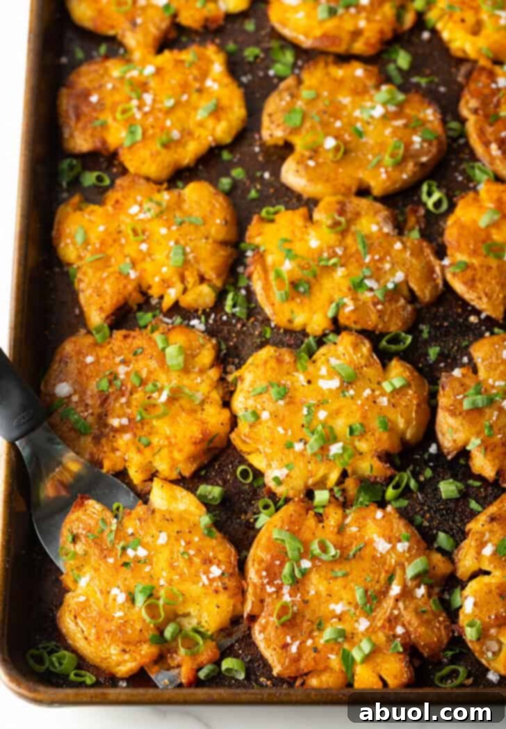 Close-up top down view of 15 golden crispy smashed potatoes on a baking sheet, glistening with butter and spices, hinting at deliciousness and inviting taste.