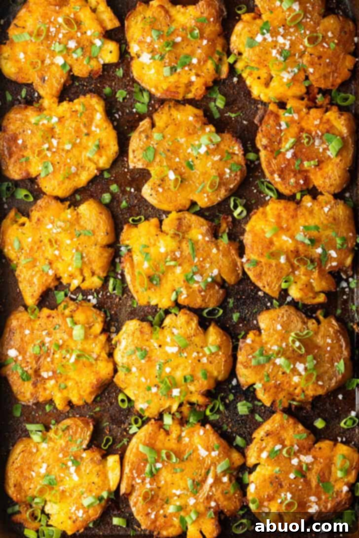 Close-up top down view of 15 perfectly golden and crispy smashed potatoes arranged on a baking sheet, glistening with butter and aromatic spices after being perfectly baked.