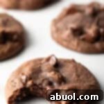 5 baked nutella cookies with chocolate chips on a white background. The closest cookie has a bite taken out of it.