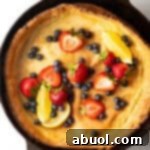 Top down view of a Dutch Baby pancake in a cast iron skillet, topped with strawberries, blueberries, and lemon slices.