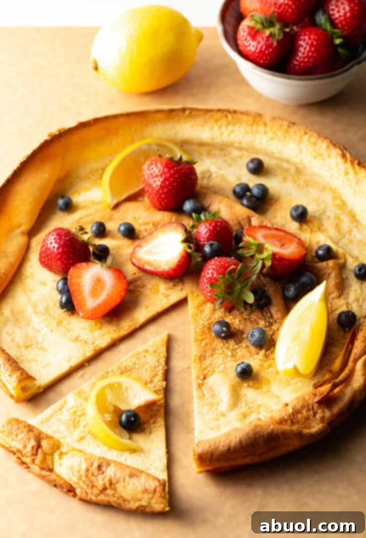 A Dutch Baby pancake presented on a wooden cutting board, adorned with fresh strawberries and blueberries. A wedge has been sliced and pulled aside, revealing the tender, layered interior.