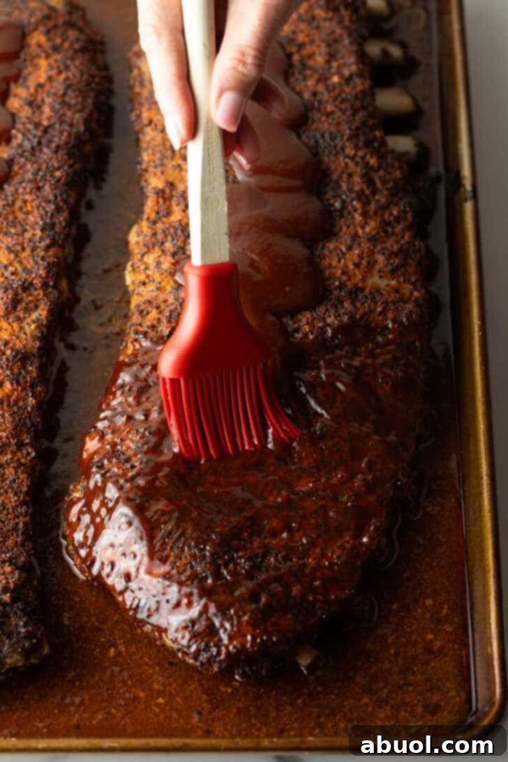 Ultimate St Louis Pork Ribs 11 St Louis-style ribs on oven tray being brushed with barbecue sauce.