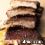Ultimate St Louis Pork Ribs 14 St. Louis style ribs stacked on top of each other on cutting board.