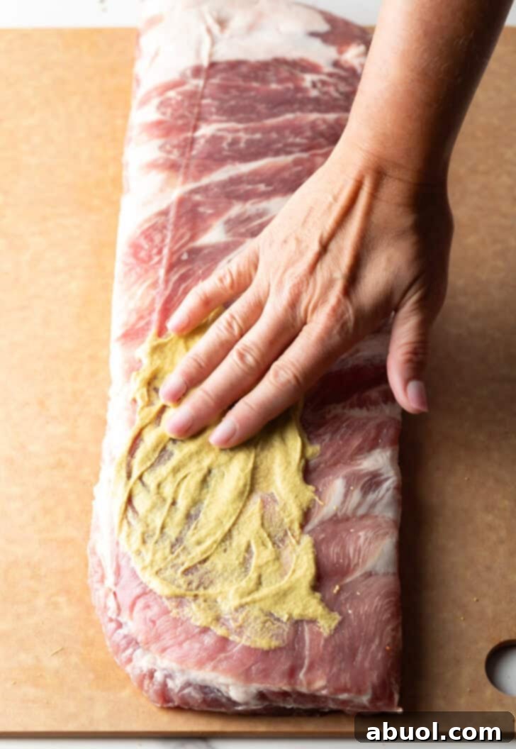 Ultimate St Louis Pork Ribs 7 Overhead shot of a raw rack of St. Louis pork ribs being smothered with Dijon mustard.