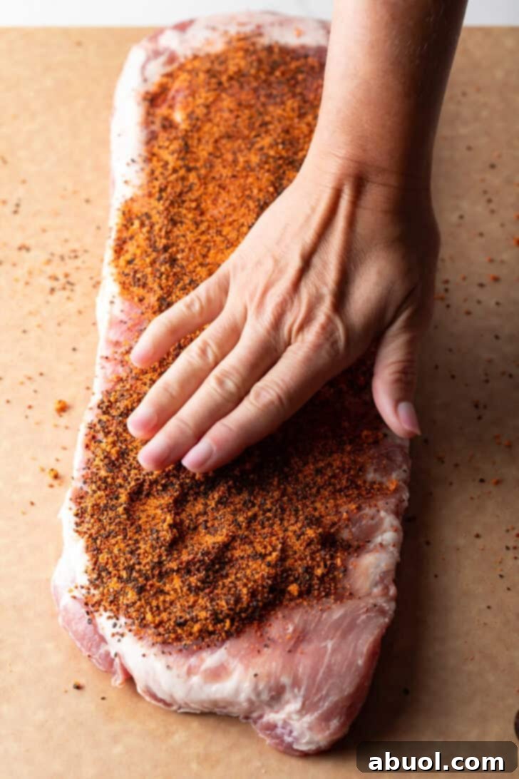 Ultimate St Louis Pork Ribs 8 Overhead shot of a raw rack of pork ribs with a hand covering it with dry rub seasoning.