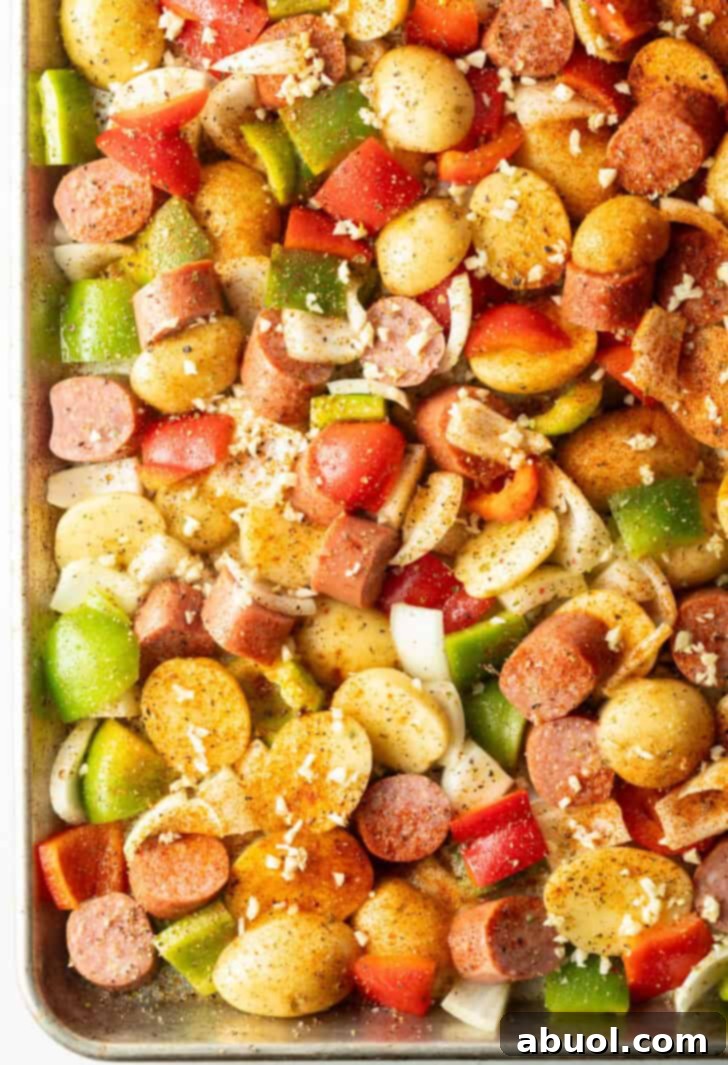 Kielbasa sausage and veggies with seasonings and garlic on a sheet pan.