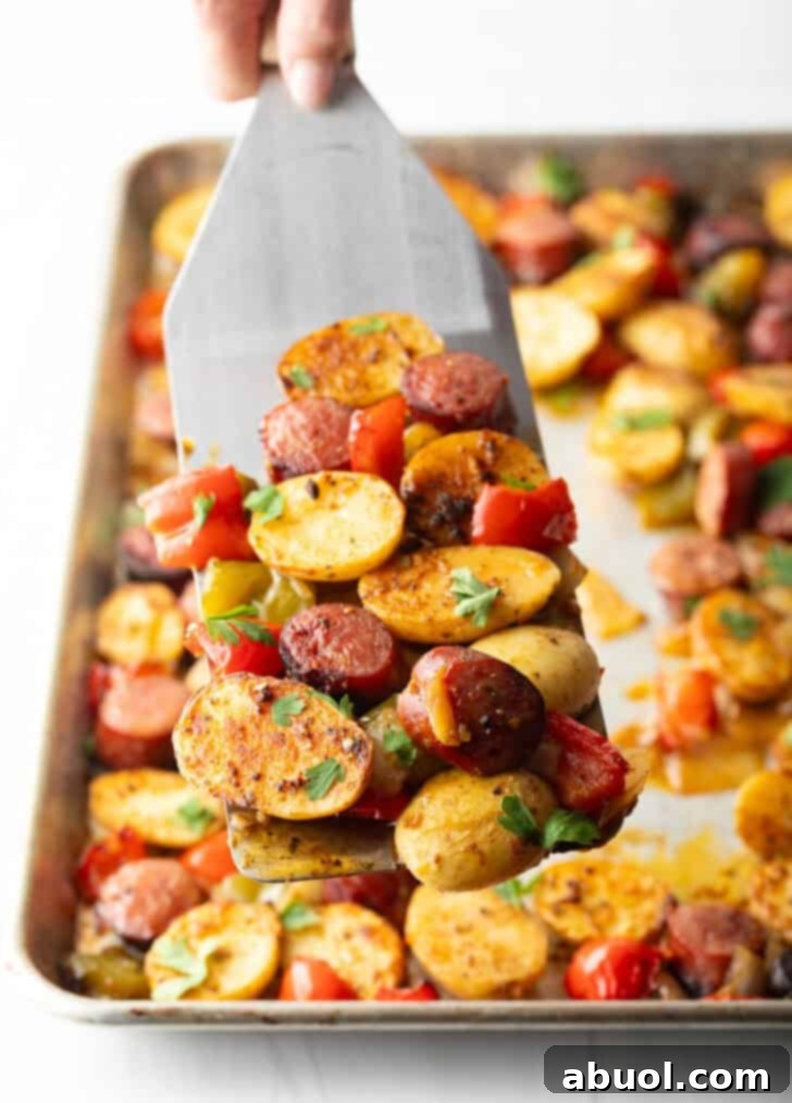 Metal spatula holding up a scoop of kielbasa and potatoes with red peppers.
