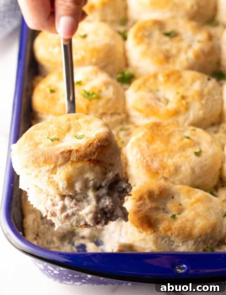A metal spatula taking a scoop of biscuits and gravy breakfast casserole from the pan, showing the rich gravy and fluffy biscuits.