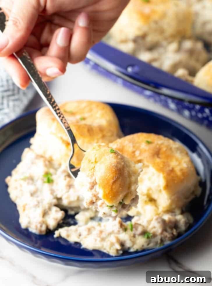 A blue plate with a serving of sausage biscuits and gravy casserole with a fork holding a bite, showing the layers of gravy and biscuit.