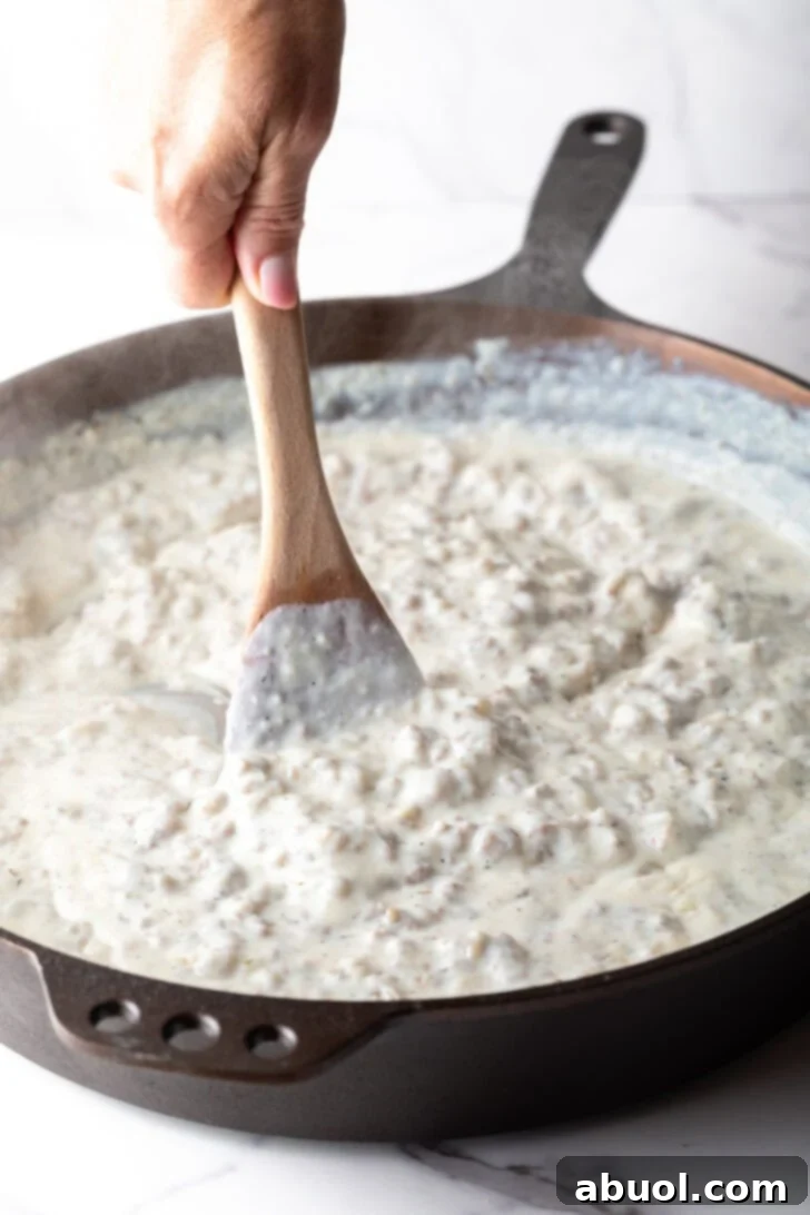 Sausage gravy being stirred with a wooden spoon in a skillet.