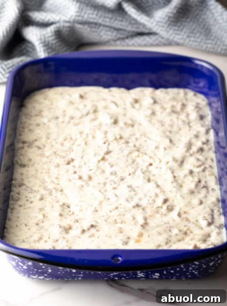 Sausage gravy layered on the bottom of a blue baking pan, ready for biscuits.