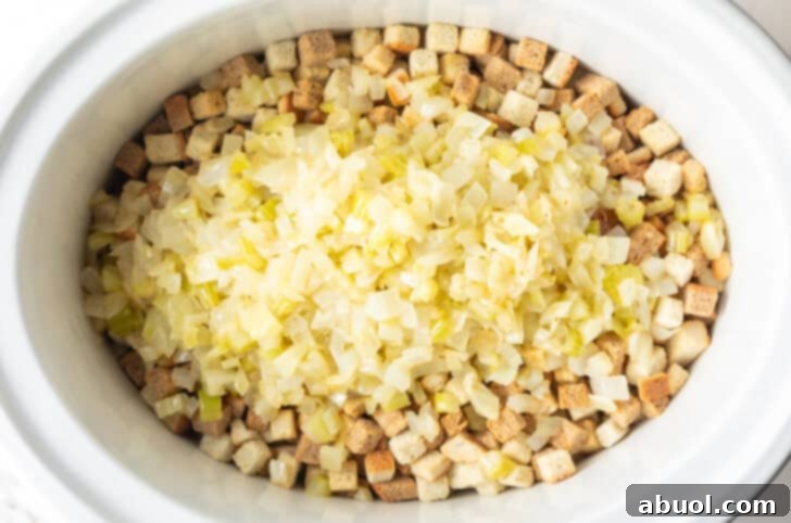 Dried bread cubes topped with cooked onions in a white crock pot.