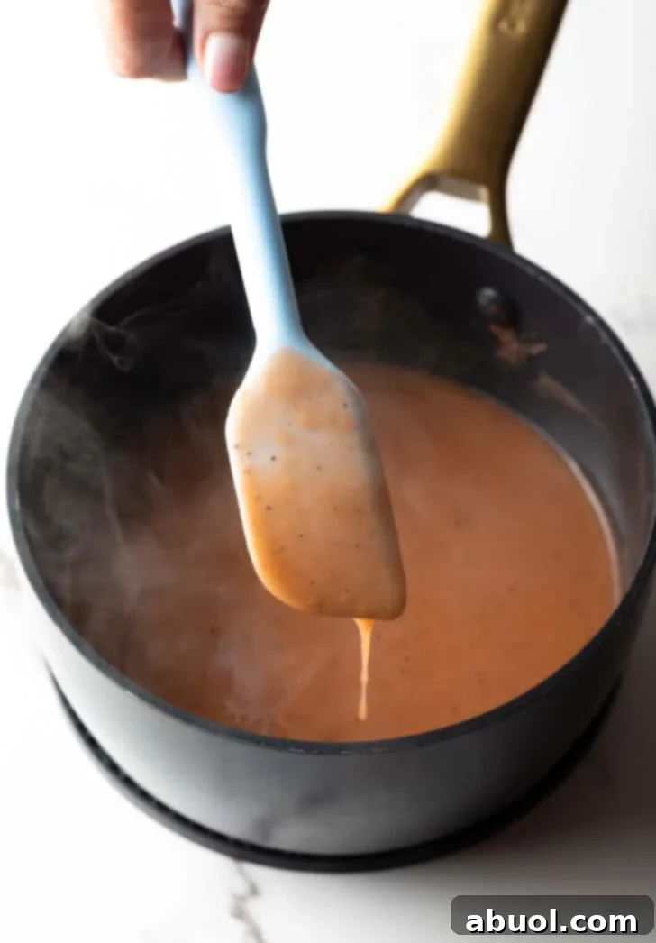 Easy gravy recipe dripping luxuriously off of a spatula over a black pot, showing its rich, thick texture.