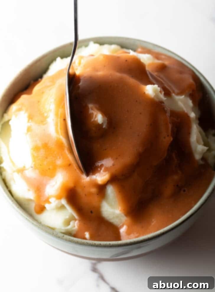 A large bowl of mashed potatoes drenched in homemade brown gravy, with a spoon ready to serve, inviting indulgence.