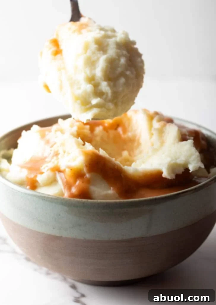 A generous scoop of mashed potatoes and gravy held over a bowl, highlighting the enticing texture and rich color.