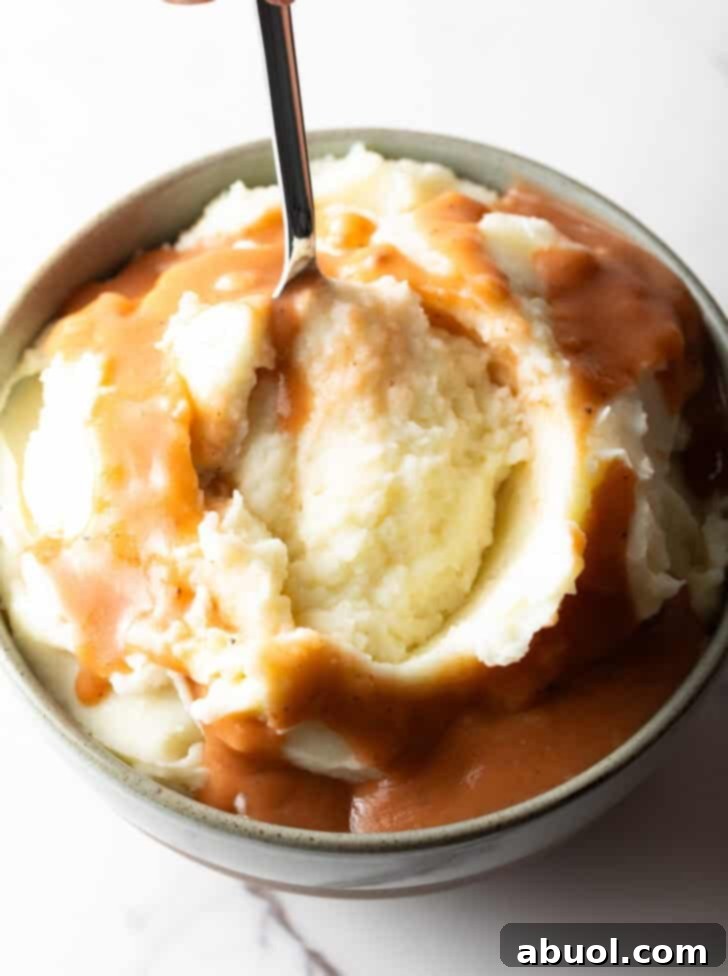 A spoon scooping a perfect bite of easy mashed potatoes and gravy from a bowl, highlighting the creamy texture.