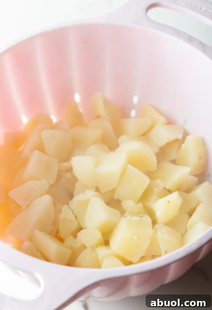 A white colander straining freshly cooked potatoes, allowing excess water to drain away.