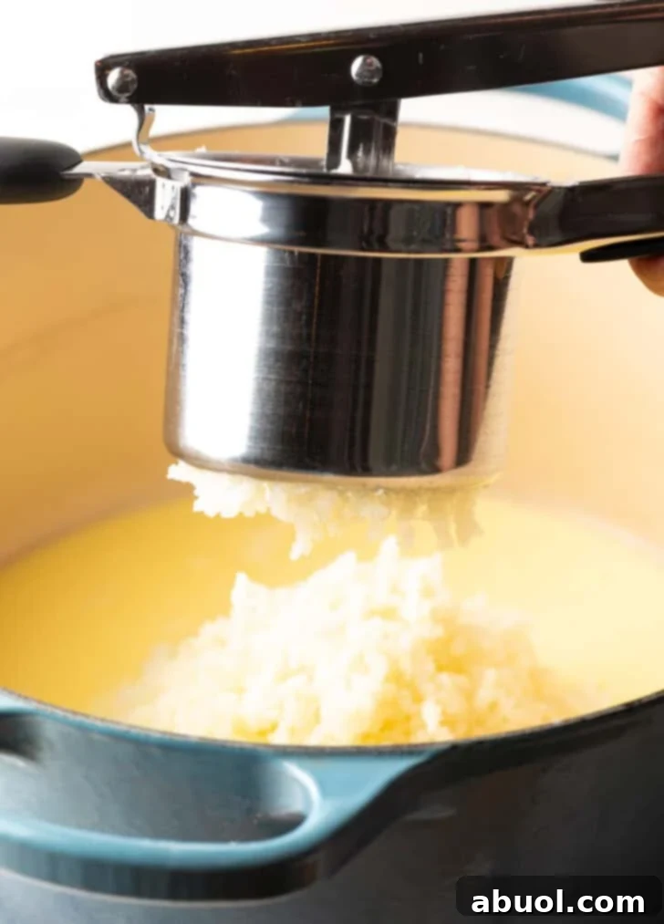 A potato ricer pressing cooked potatoes into a large pot, demonstrating the smooth mashing technique.