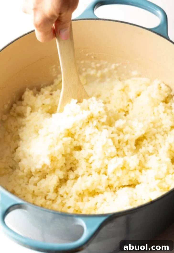 A wooden spoon stirring freshly riced potatoes in a pot, illustrating the initial mixing stage.