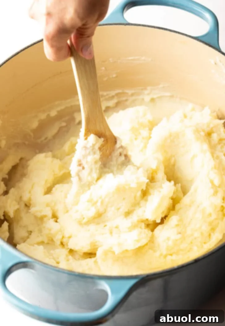 A wooden spoon stirring fully combined easy mashed potatoes, showing the creamy, fluffy texture.