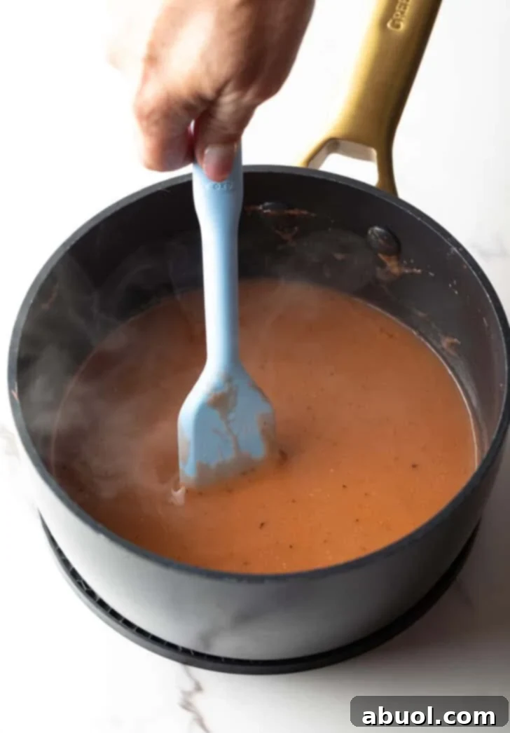 Easy brown gravy recipe being vigorously stirred by a spatula in a black pot, ensuring a smooth consistency.