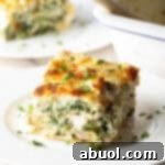 A square portion of Chicken Alfredo lasagna served on a white plate, highlighting its creamy layers and golden cheese.