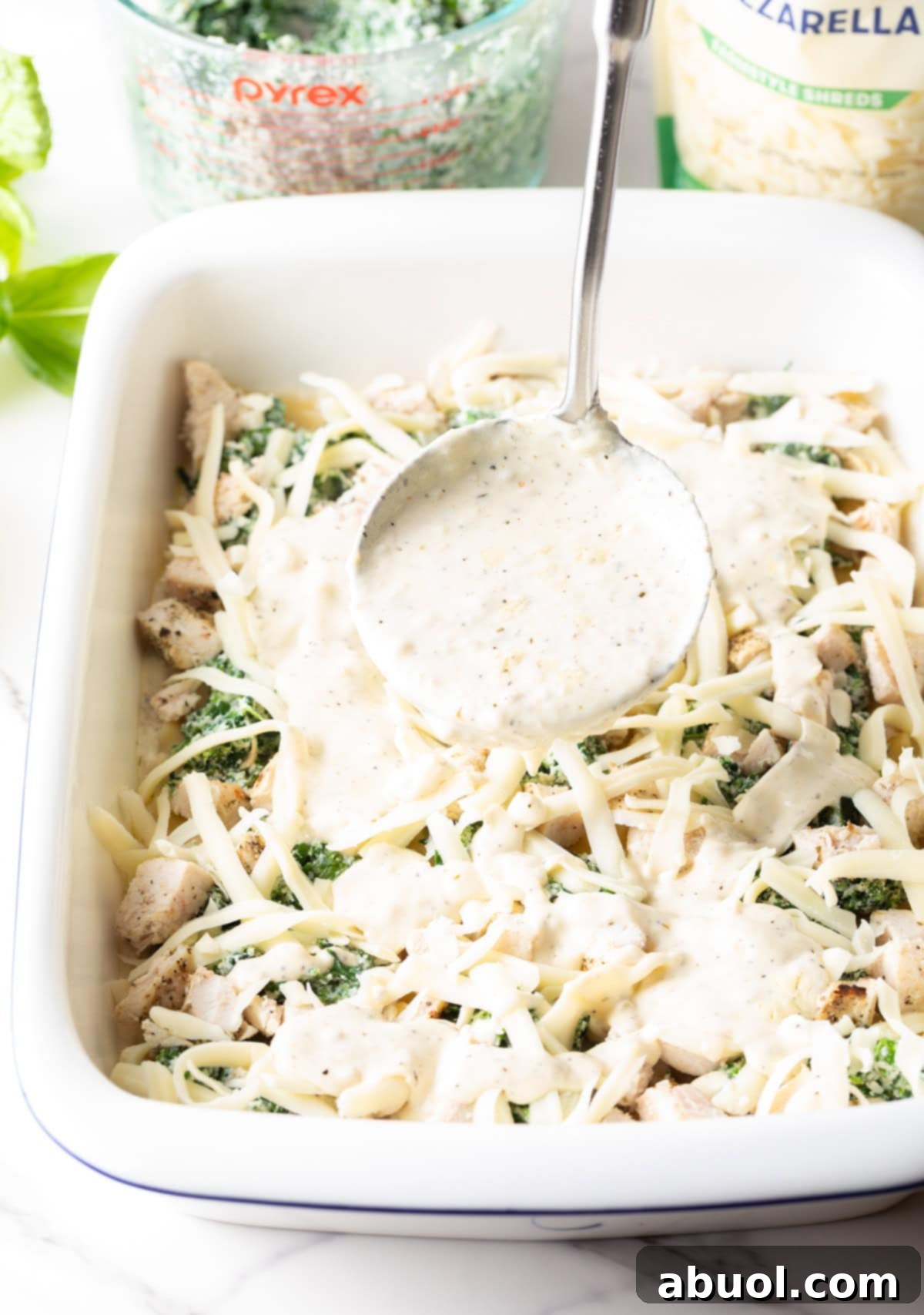 A ladle carefully pours creamy Alfredo sauce over the partially assembled lasagna in a baking dish, enhancing its rich layers.