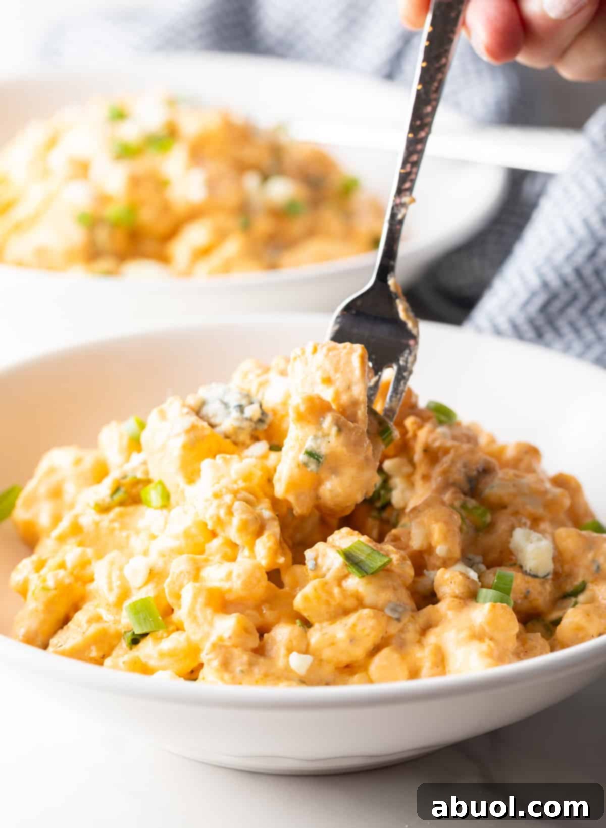 Fork taking a bite of creamy buffalo chicken mac and cheese from a white bowl.