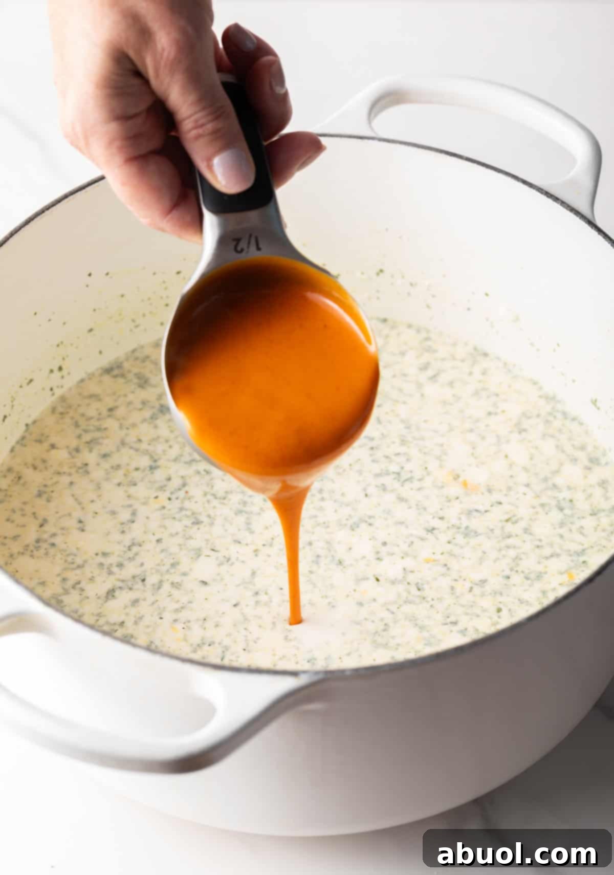 Hand pouring buffalo sauce into a large pot.