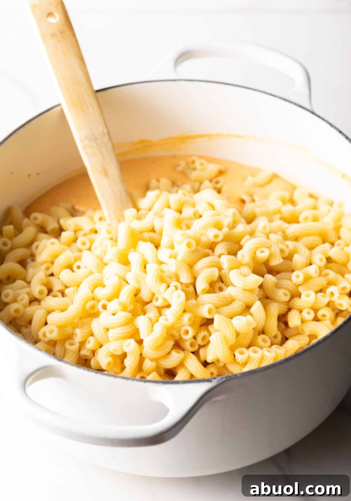 Stirring macaroni noodles into cheese sauce.