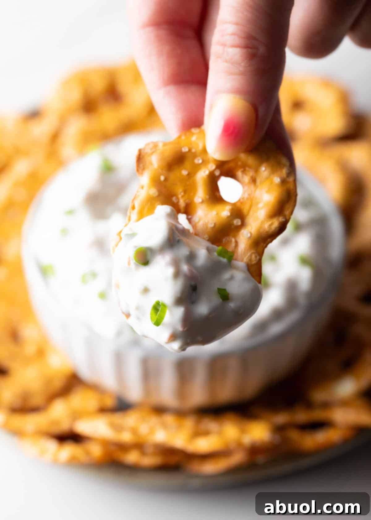 Hand holding a pretzel with a scoop of olive dip to camera.
