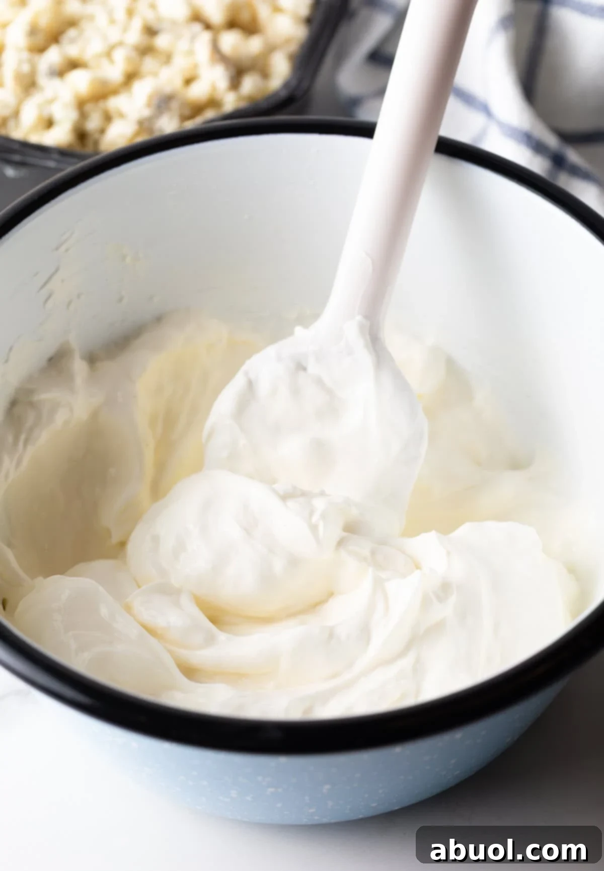 White bowl with cream cheese and olive dip, stirred with a white spatula.
