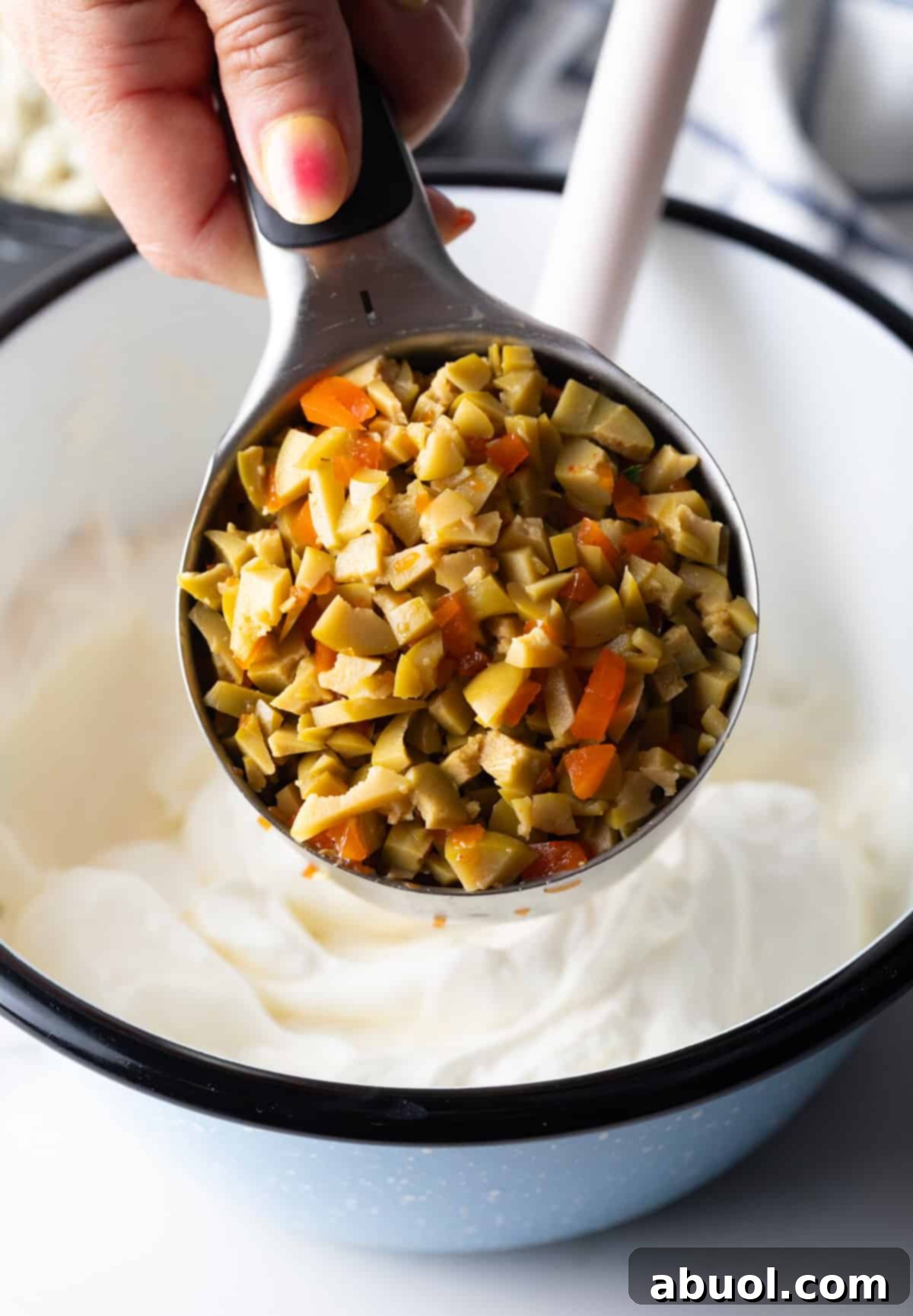 Holding a measuring cup filled with chopped olives to camera.