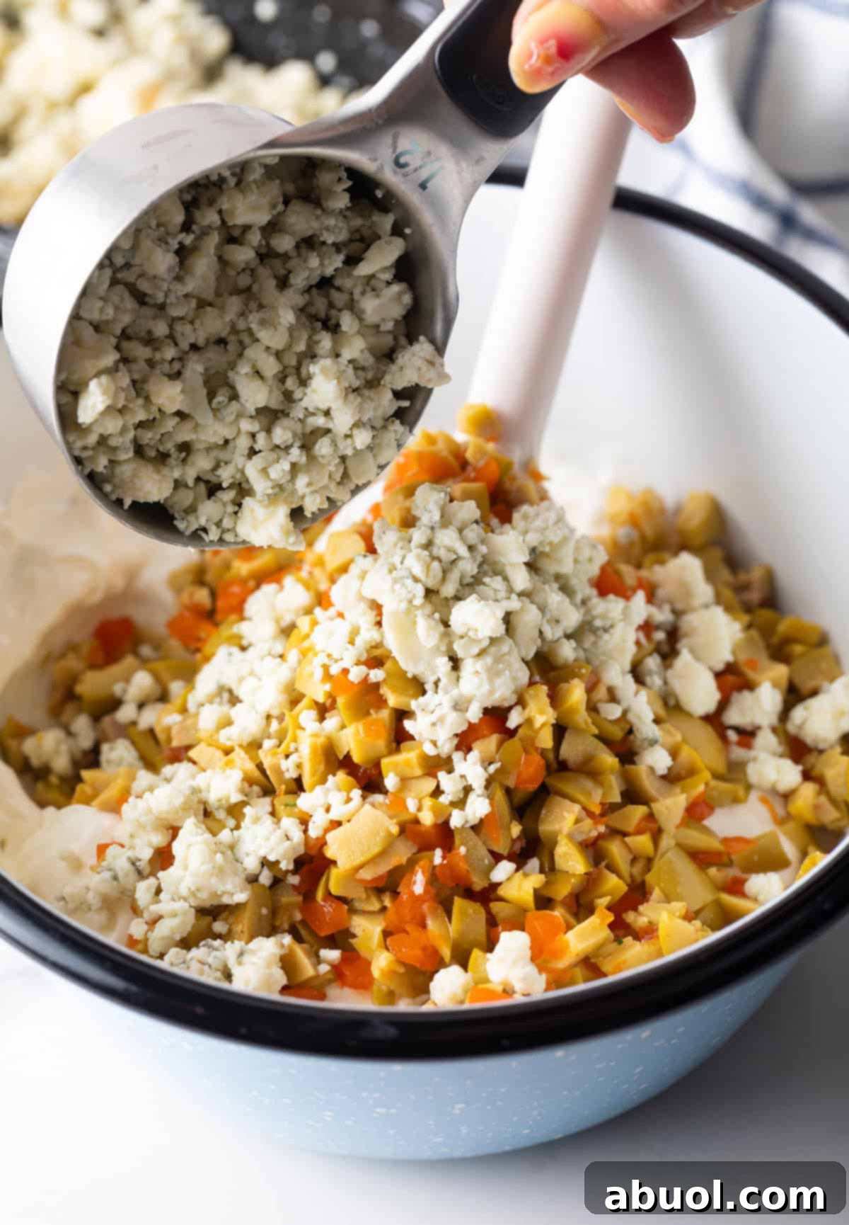 Adding crumbled blue cheese to a bowl of chopped olives, and sour cream and cream cheese.