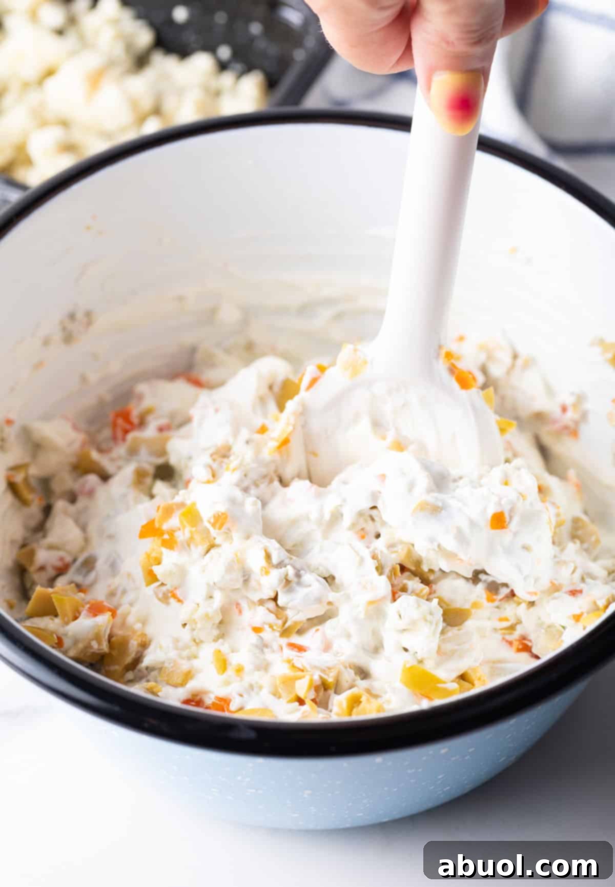 Stirring olive dip ingredients together with a white spatula.