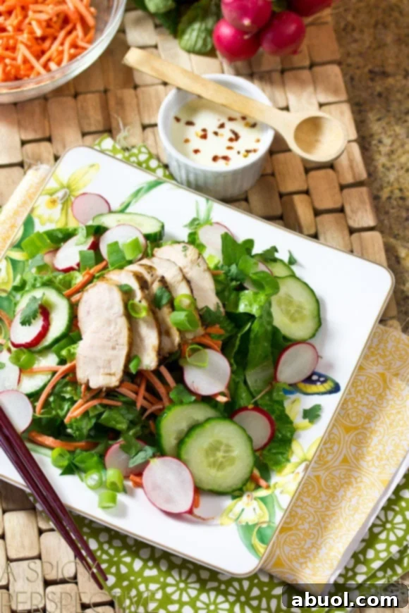 White square plate of Banh Mi Salad with fresh salad greens, sliced cucumbers and radishes, shredded carrots, and slices of grilled chicken breast, drizzled with creamy dressing.