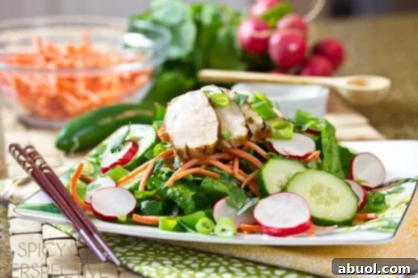 Vietnamese banh mi salad: Greens, sliced cucumbers and radishes, shredded carrots, and slices of grilled chicken breast loaded onto a white plate, ready to be served.