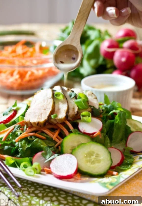 Drizzling creamy Vietnamese dressing over a plate of salad with sliced cucumbers and radishes, shredded carrots, and slices of grilled chicken breast.