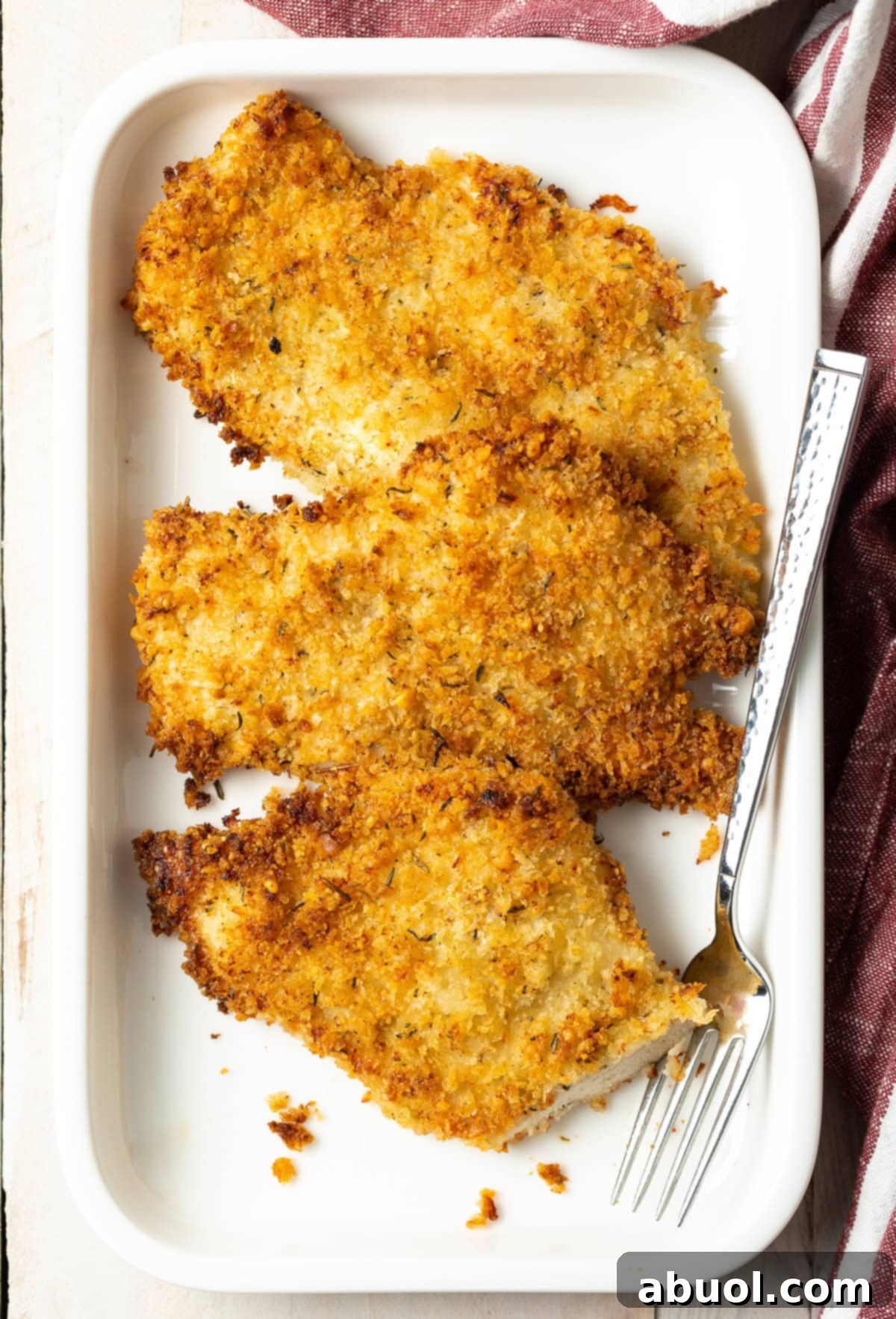 Overhead view of several perfectly oven-fried chicken cutlets on a platter, garnished with fresh herbs and a lemon wedge, ready to serve.