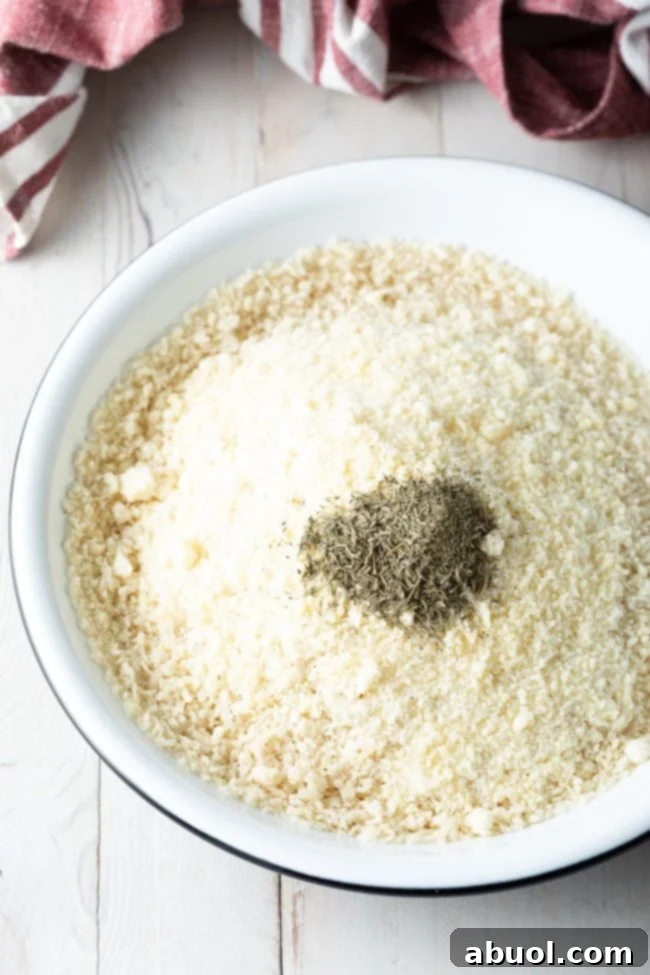 Closeup of a bowl containing Panko breadcrumbs, shredded Parmesan cheese, and fresh thyme leaves, mixed together.