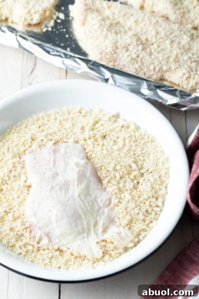 A chicken cutlet being evenly coated in the savory Panko breadcrumb mixture after being dipped in mayonnaise.
