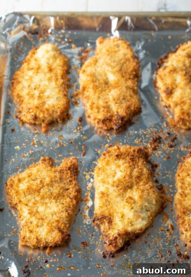 An overhead shot of several crispy baked chicken cutlets resting on a non-stick foil-lined baking tray, fresh from the oven and perfectly golden.