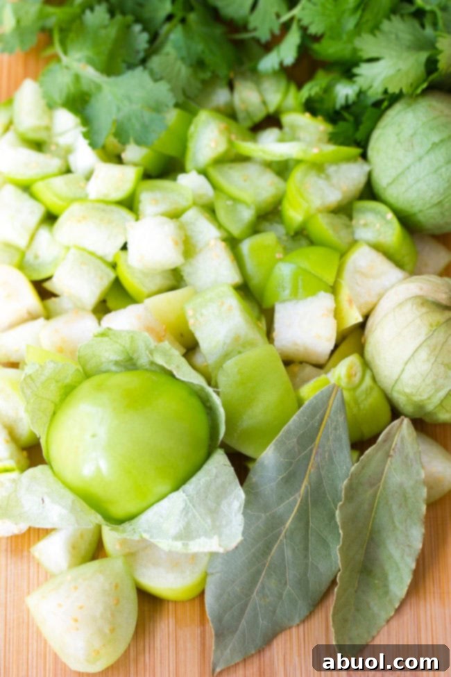 Diced tomatillos on a cutting board with cilantro and bay leaves. 