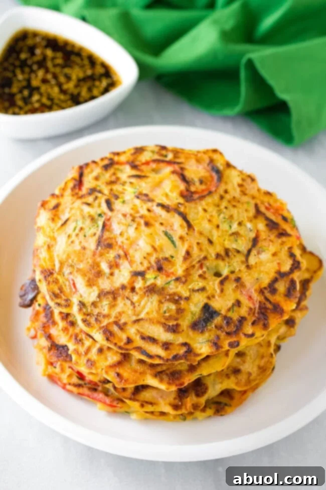 Pajeon #ASpicyPerspective #KoreanPancakes #KoreanPancakeRecipe #Pajun #Pajeon #Korean #Vegetarian A neatly stacked arrangement of golden-brown scallion veggie pancakes (Pajeon) on a white plate after being perfectly cooked, highlighting their appealing texture.
